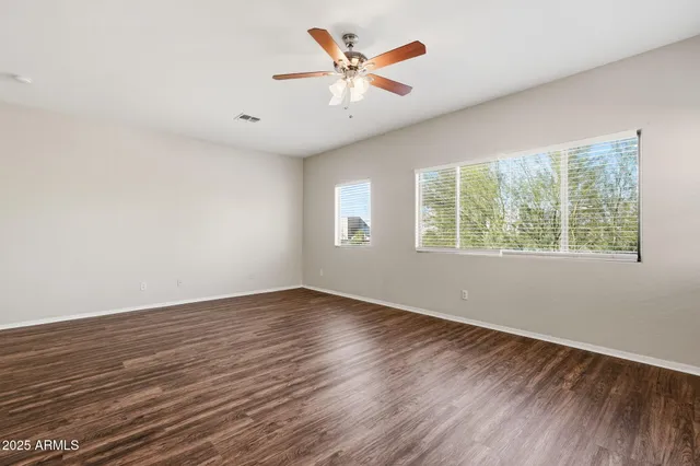 an empty room with wooden floor chandelier fan and windows
