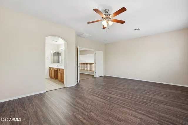 an empty room with wooden floor chandelier fan and windows