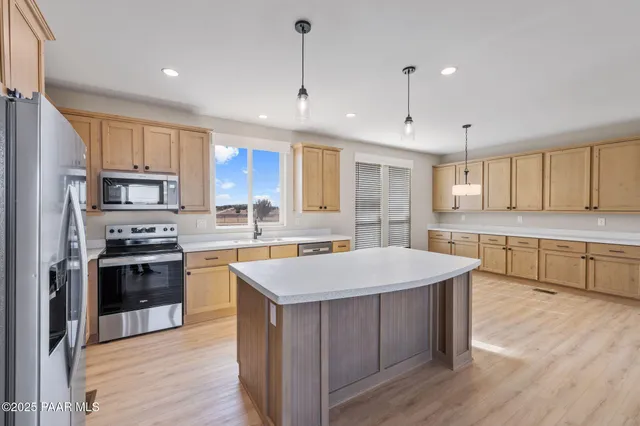 a large kitchen with stainless steel appliances kitchen island granite countertop a stove a sink a refrigerator and white cabinets with wooden floor