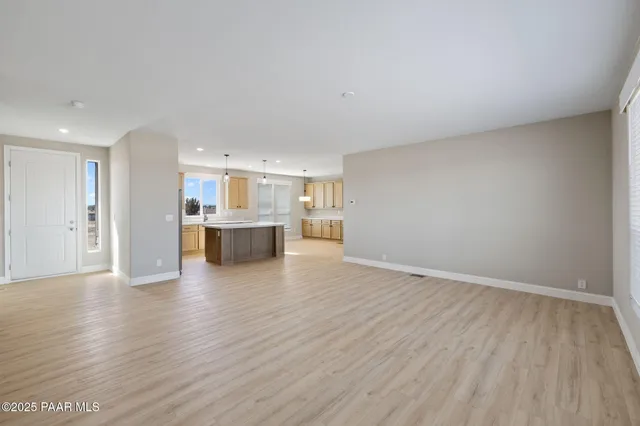 a view of a kitchen and an empty room with wooden floor and a kitchen