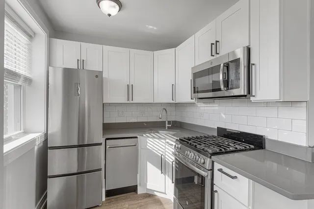 a kitchen with stainless steel appliances granite countertop white cabinets a refrigerator a sink a stove a microwave and wooden floors