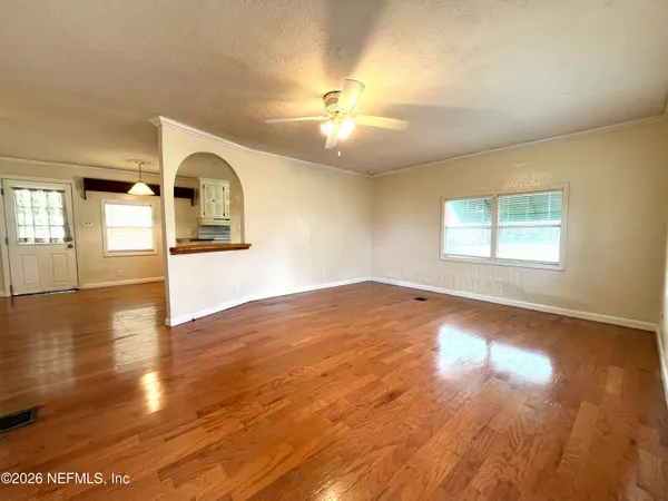 an empty room with a chandelier fan and wooden floor