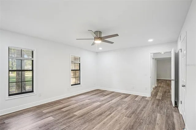 an empty room with wooden floor fan and windows