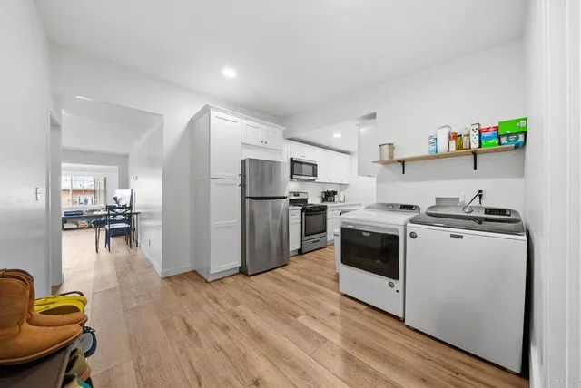 a kitchen with stainless steel appliances a refrigerator a stove a sink dishwasher and white cabinets with wooden floor