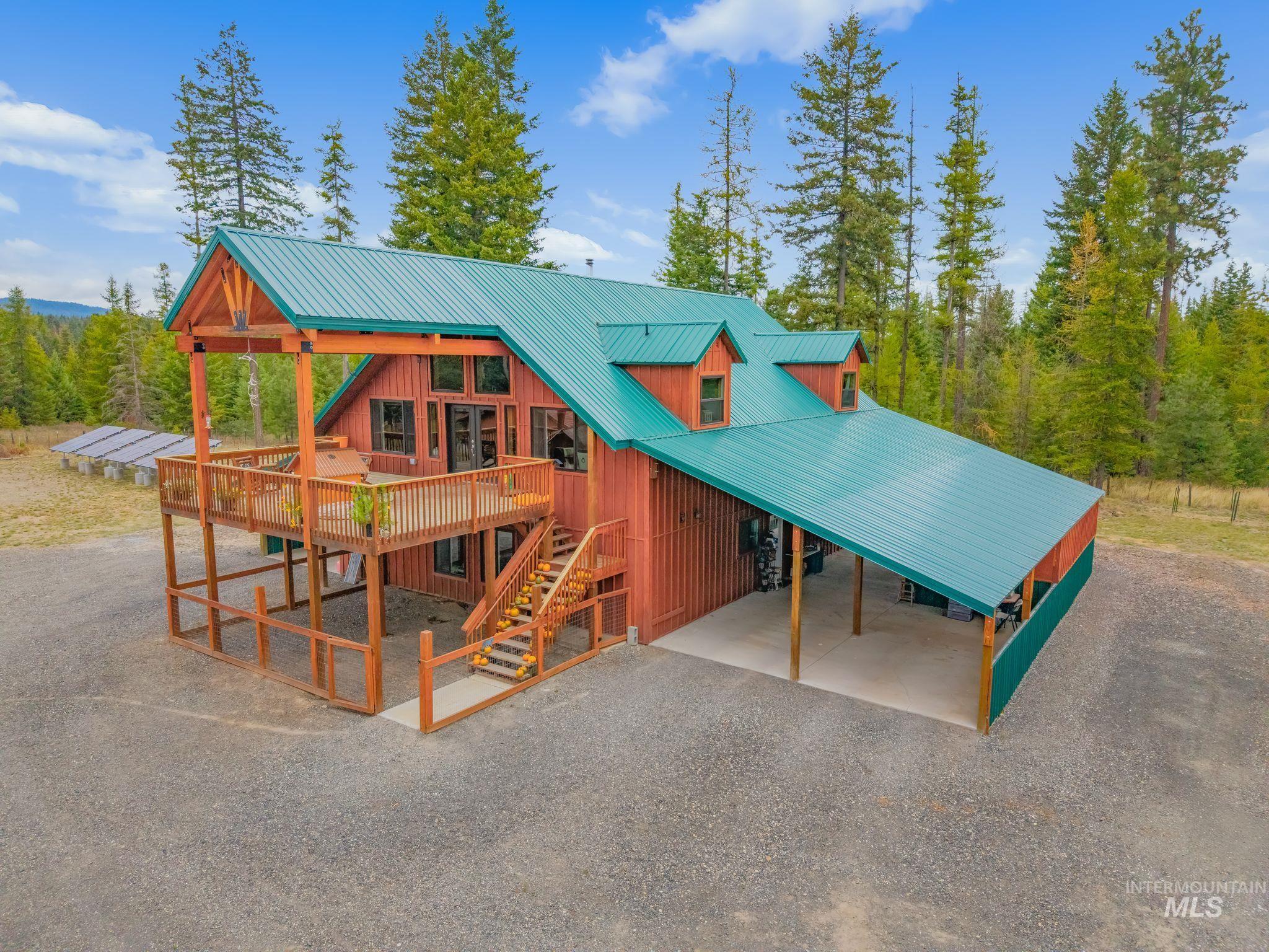 3989 East Mountain Road Anatone, WA 99401 - Photo 1 of 49 Red-sided residence featuring a teal metal roof, a multi-level wood deck, an exterior staircase, and an attached covered parking area