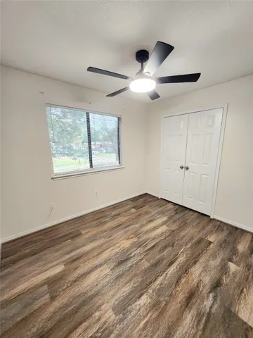 an empty room with wooden floor ceiling fan and windows