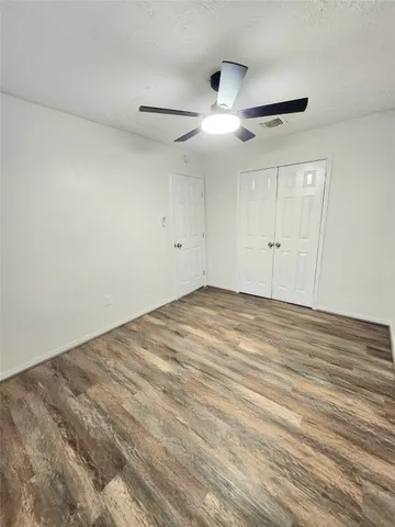 an empty room with wooden floor ceiling fan and windows