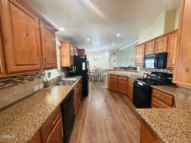 a large kitchen with stainless steel appliances granite countertop a stove top oven a sink dishwasher a dining table and chairs with wooden floor