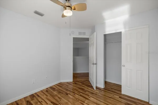 an empty room with wooden floor fan and windows