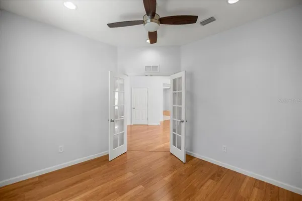 an empty room with wooden floor ceiling fan and windows