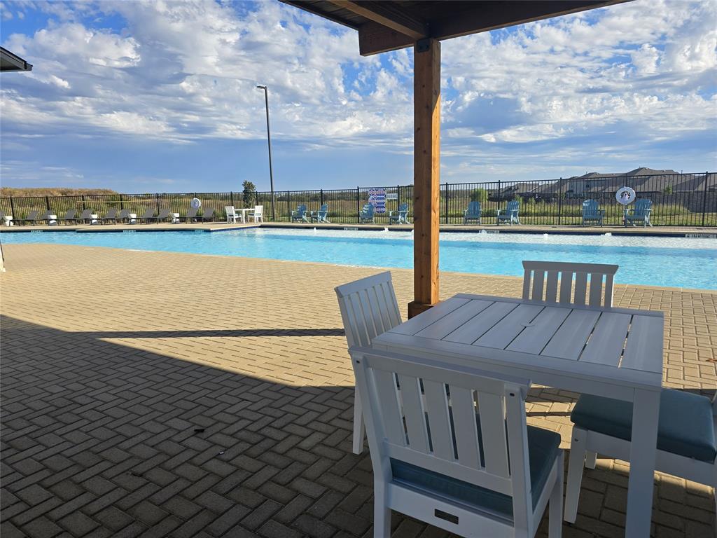 Expansive outdoor pool area featuring a large swimming pool, herringbone-patterned paver decking, a wood pergola structure, and perimeter fencing