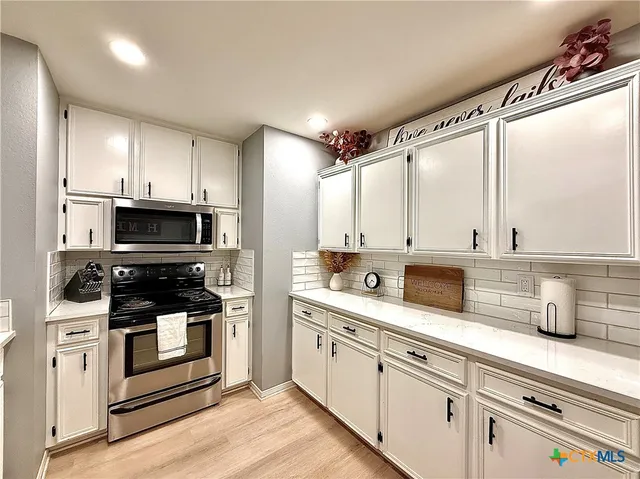 a kitchen with stainless steel appliances granite countertop a stove a sink and white cabinets