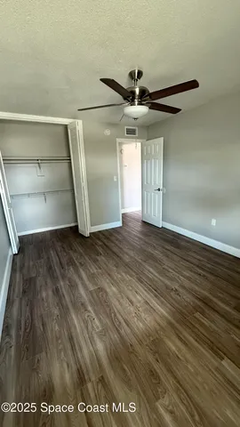 an empty room with wooden floor closet fan and windows