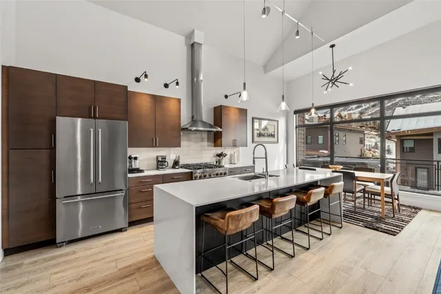 a kitchen with stainless steel appliances a refrigerator a stove a sink a dining table and chairs with wooden floor