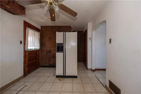a view of a refrigerator in kitchen and an empty room with wooden floor