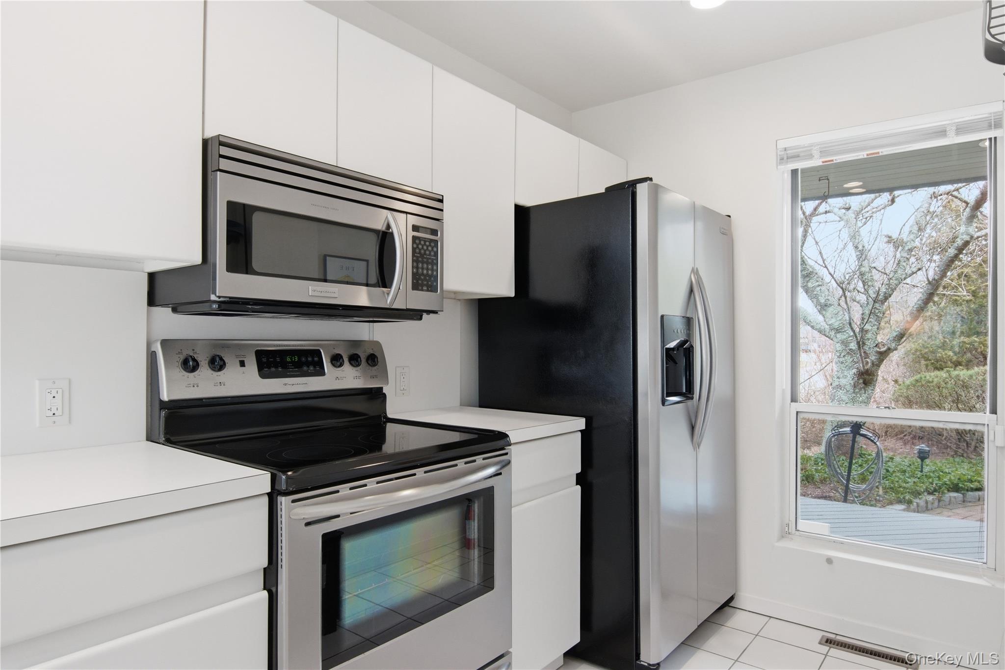 23 Library Avenue, Unit 1 Westhampton Beach, NY 11978 - Photo 3 of 24 Kitchen with stainless steel appliances, light countertops, white cabinets, and light tile patterned floors