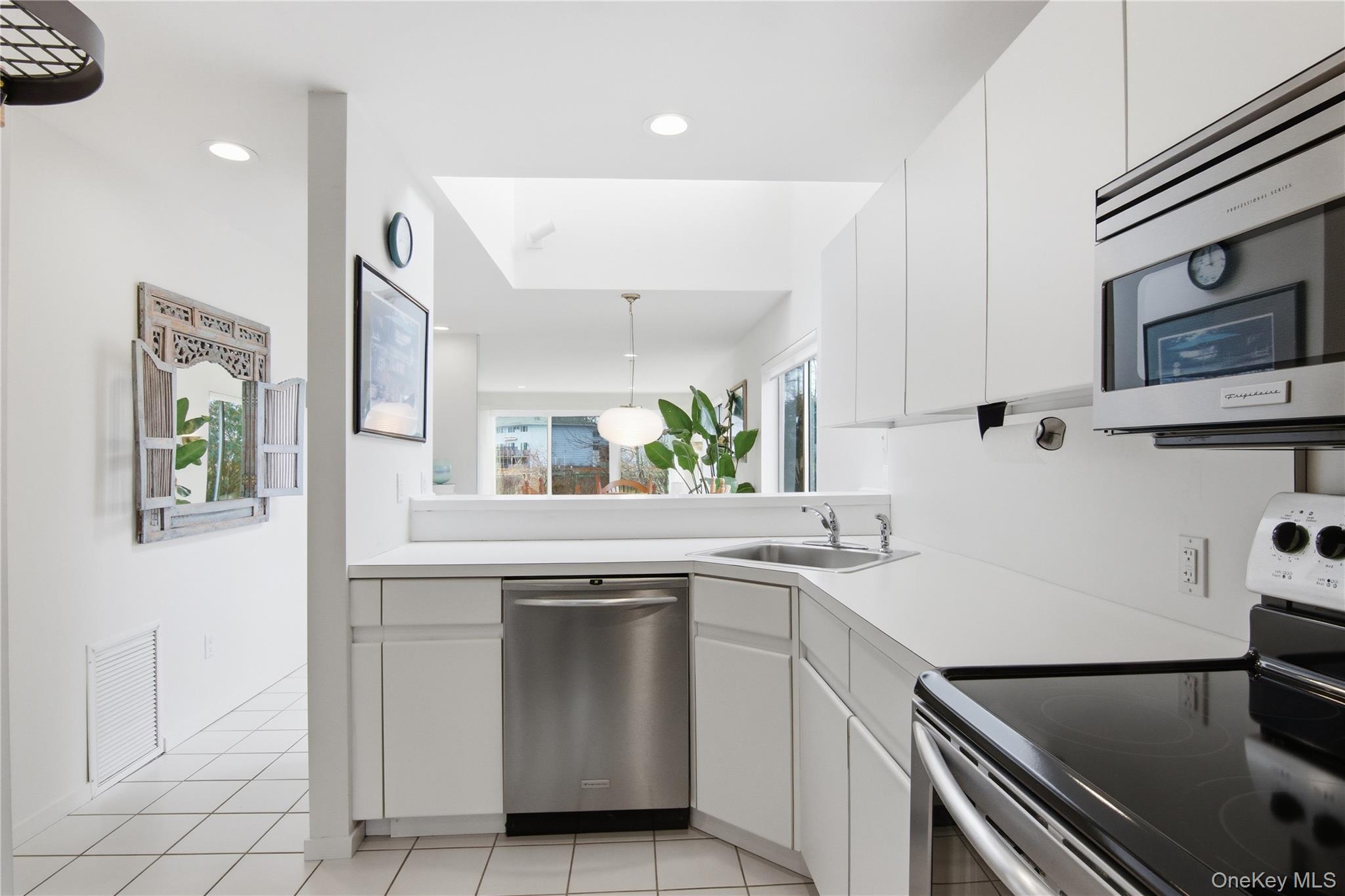 23 Library Avenue, Unit 1 Westhampton Beach, NY 11978 - Photo 5 of 24 Kitchen featuring stainless steel appliances, white cabinets, light countertops, light tile patterned floors, and decorative light fixtures