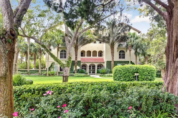 a view of a white house with a big yard and potted plants and large trees
