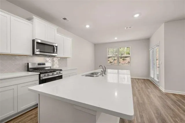 a kitchen with stainless steel appliances a stove a sink a microwave a refrigerator a cabinets and wooden floor