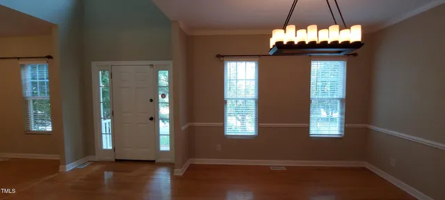 an empty room with wooden floor chandelier and windows