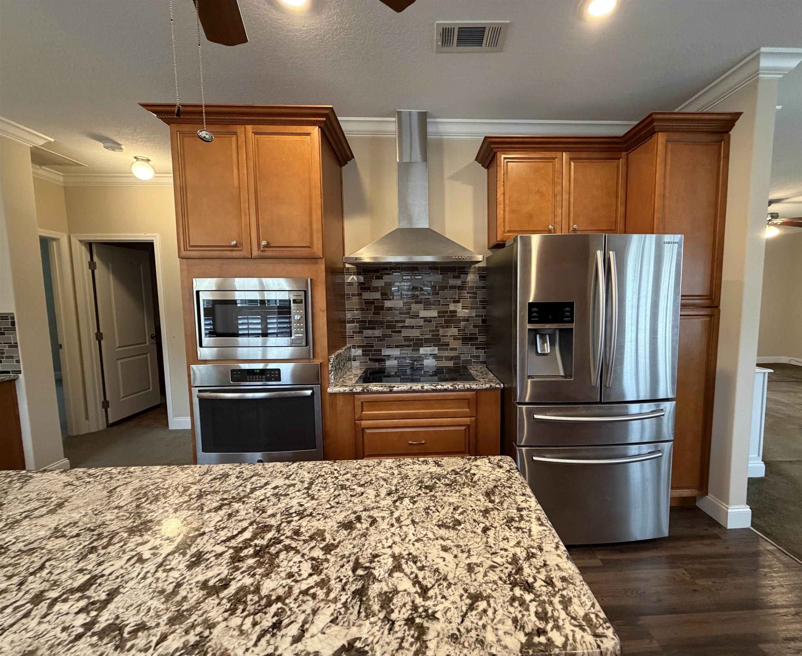 2434 Pellicer Road St. Augustine, FL 32092 - Photo 13 of 41 Kitchen with a ceiling fan, brown cabinets, appliances with stainless steel finishes, wall chimney range hood, and light stone countertops