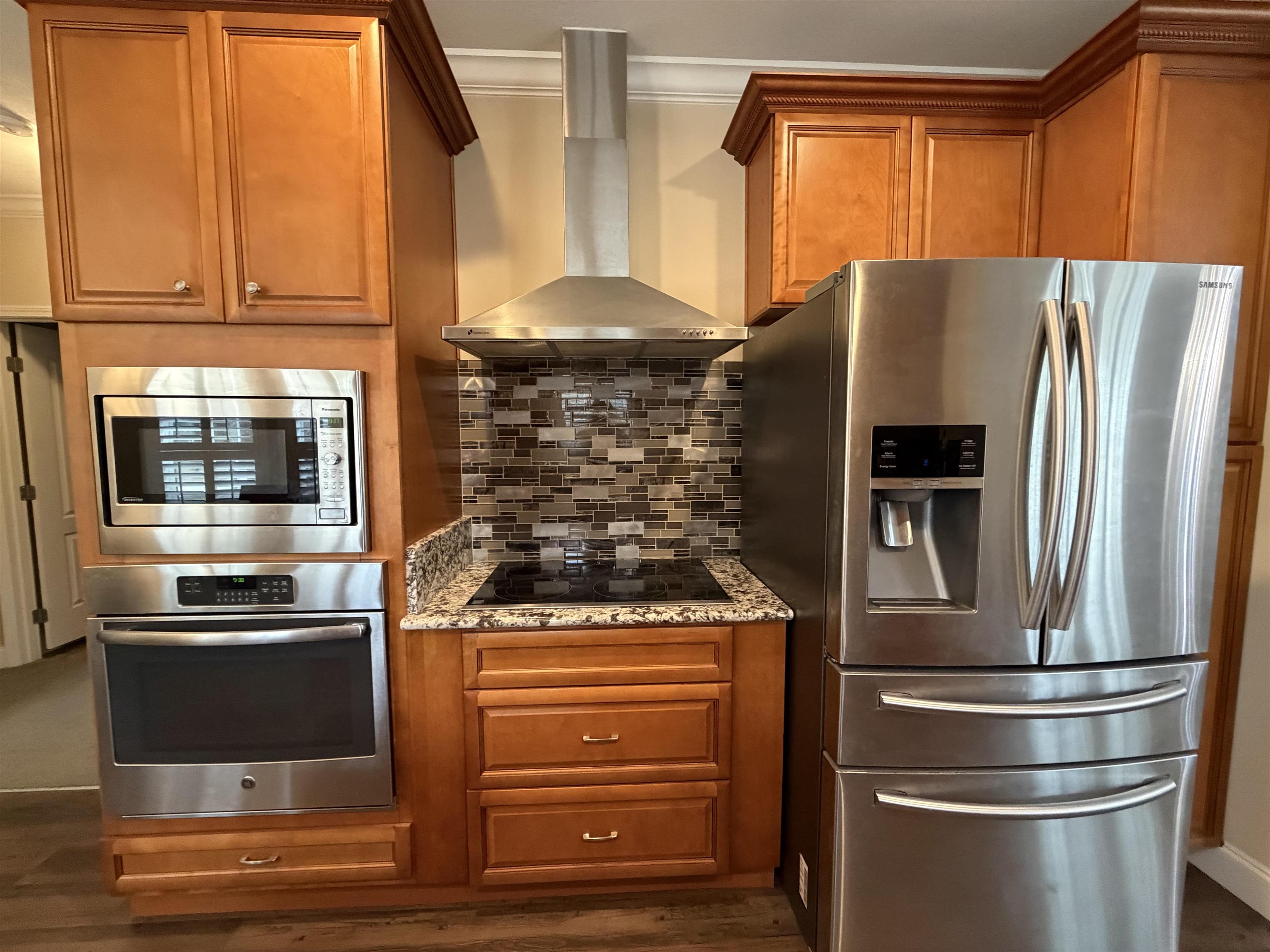 2434 Pellicer Road St. Augustine, FL 32092 - Photo 8 of 41 Kitchen featuring appliances with stainless steel finishes, wall chimney range hood, brown cabinetry, light stone counters, and crown molding