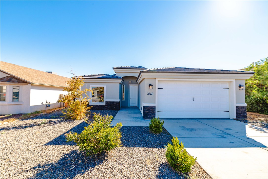 3640 North Kenneth Road Kingman, AZ 86409 - Photo 1 of 44 View of front of property featuring stone siding, concrete driveway, stucco siding, an attached garage, and a tile roof