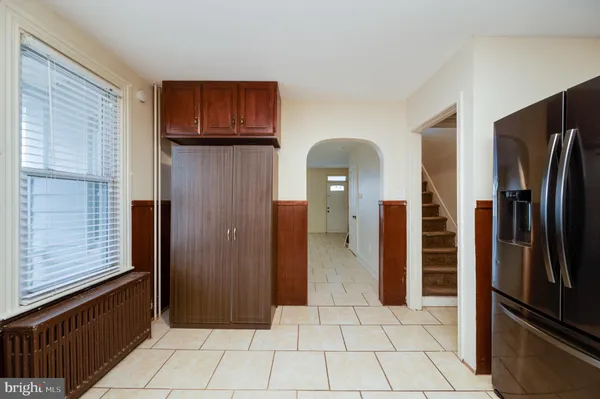 a view of a refrigerator in kitchen and an empty room with wooden floor