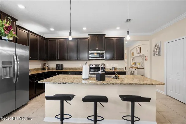 a kitchen with stainless steel appliances kitchen island granite countertop a refrigerator a stove a sink and chairs