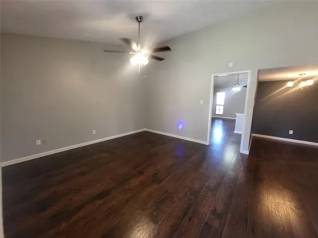 a view of an empty room with wooden floor and a ceiling fan
