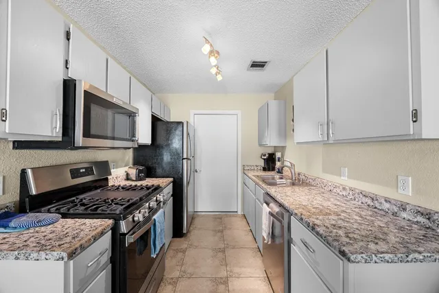 a kitchen with stainless steel appliances granite countertop a stove top oven a sink dishwasher and a refrigerator with wooden cabinets