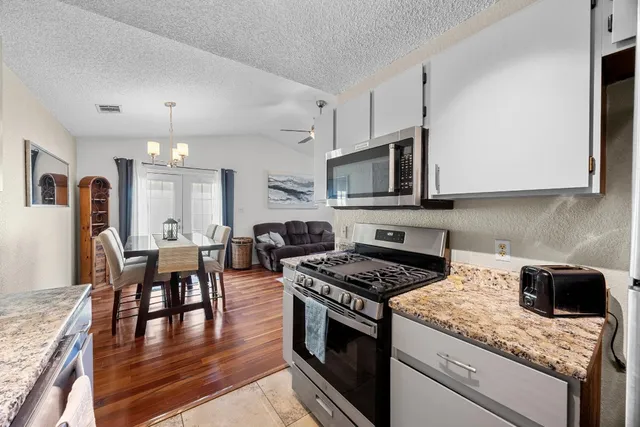 a kitchen with granite countertop stainless steel appliances a stove a sink a microwave a dining table and chairs with wooden floor