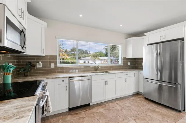 a kitchen with granite countertop stainless steel appliances a stove a sink a refrigerator and cabinets