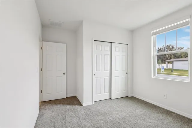 a view of an empty room with window and kitchen view