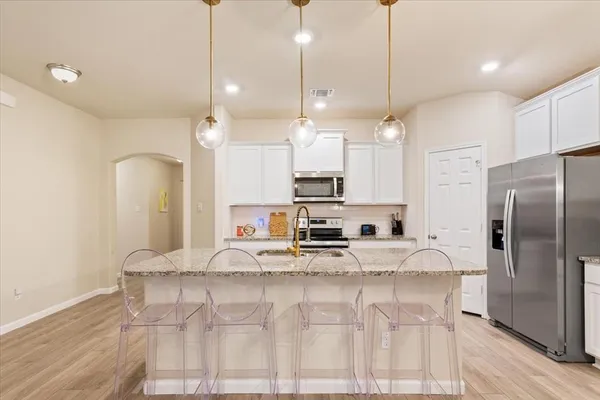 a kitchen with kitchen island granite countertop a table chairs refrigerator and microwave