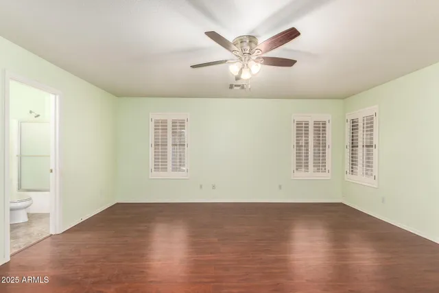 an empty room with wooden floor fan and windows