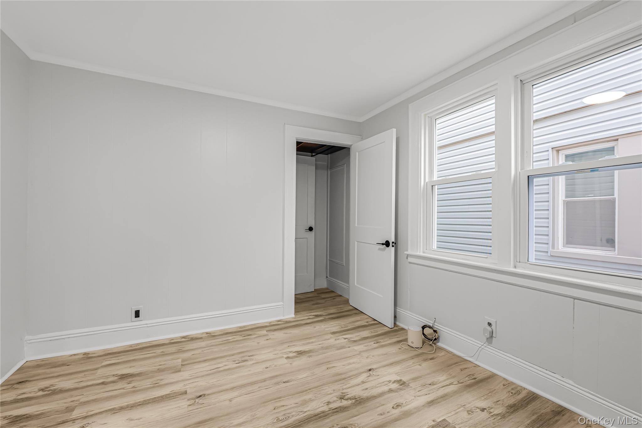 173-43 103rd Road Queens, NY 11433 - Photo 24 of 43 Wood-finish flooring, white trim, two white-framed windows, and a white interior door with black hardware