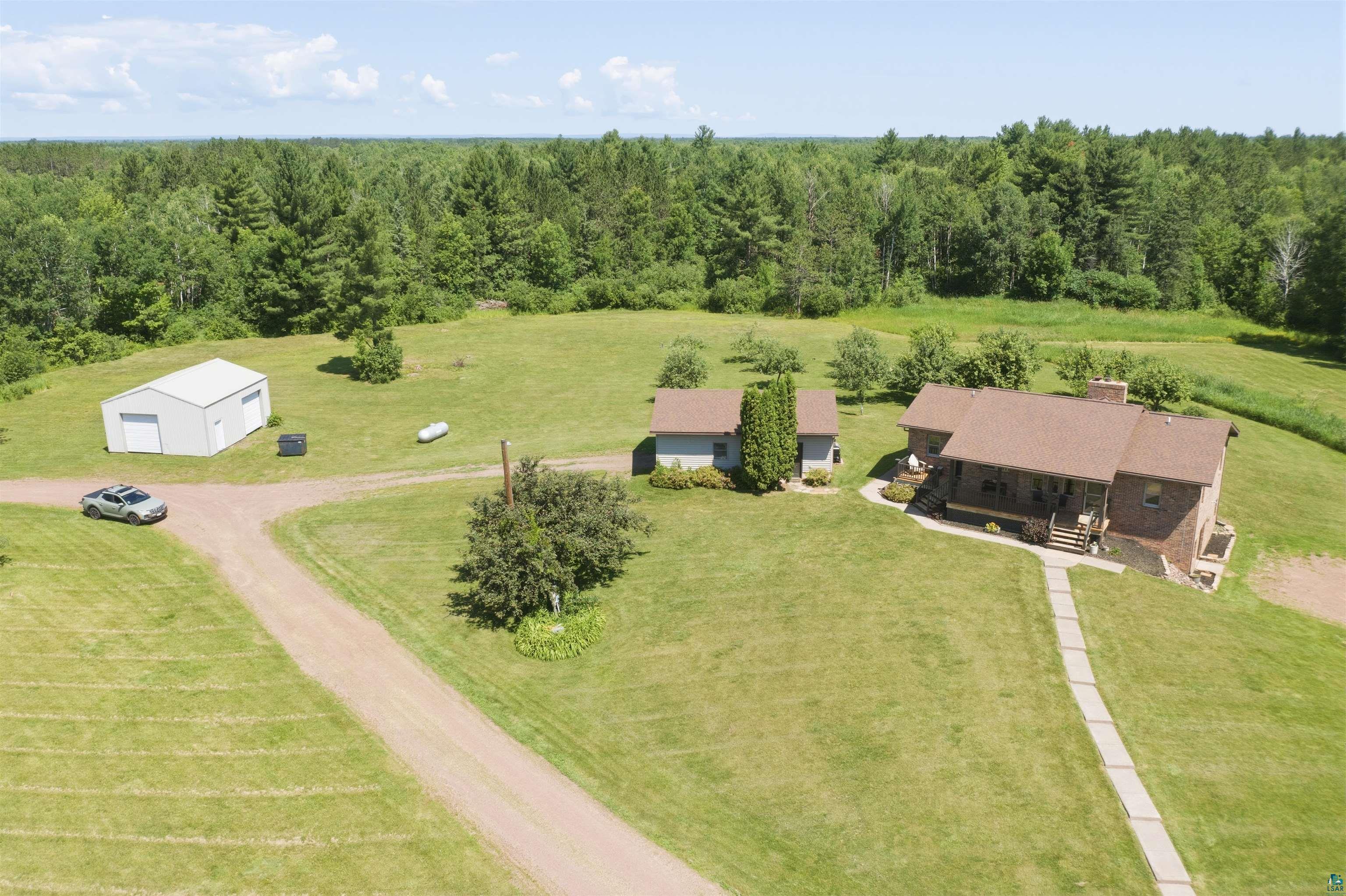 64260 Jolma Road Ashland, WI 54806 - Photo 5 of 35 Expansive property featuring a brick residence with a brown shingle roof, a separate detached garage with two bays, and additional outbuildings