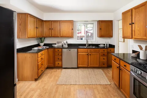 a kitchen with stainless steel appliances granite countertop wooden cabinets a sink a stove a refrigerator and island with wooden floor