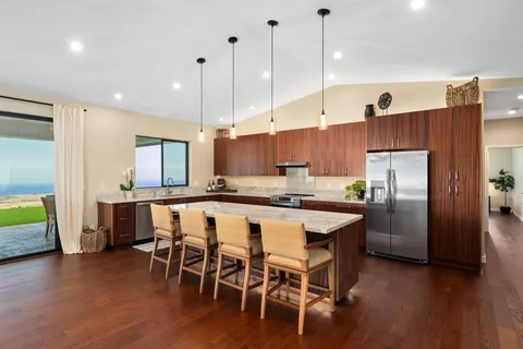 a large kitchen with stainless steel appliances a large counter top a stove a sink dishwasher a refrigerator and a oven with wooden floor