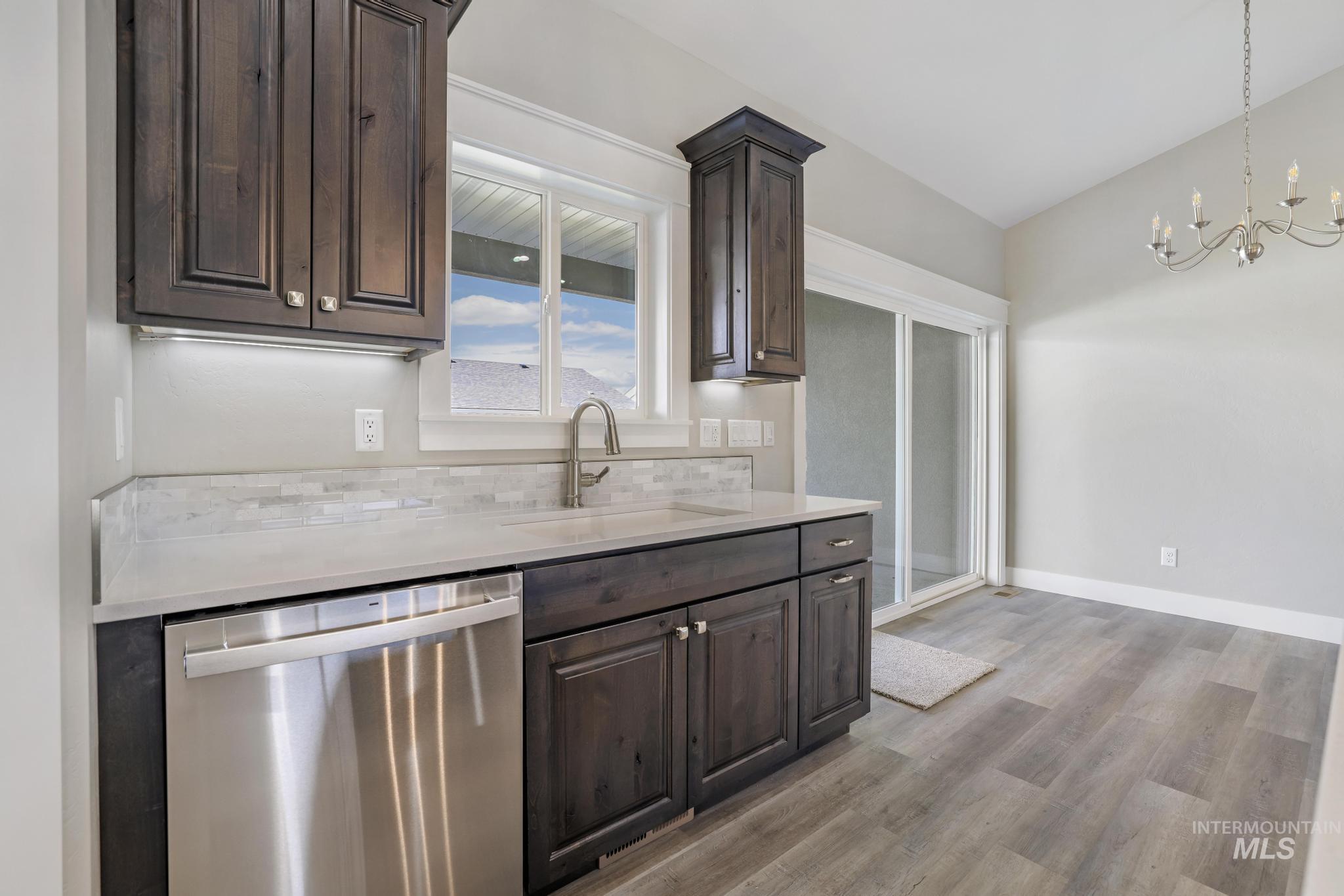 298 Sandi Road Twin Falls, ID 83301 - Photo 4 of 24 Dark wood-finish cabinetry with polished hardware, light-toned countertops, a stainless steel dishwasher, a window over the sink, and wood-finish flooring