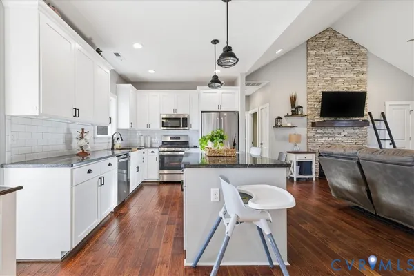 a kitchen with stainless steel appliances granite countertop a stove top oven a sink dishwasher a dining table and chairs with wooden floor