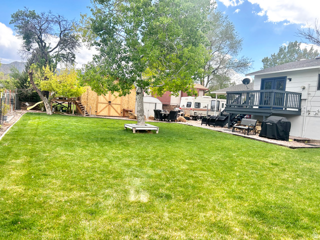 570 250 East Parowan, UT 84761 - Photo 25 of 27 Spacious rear yard featuring an expansive lawn, mature trees, and a raised wood deck with dark railing