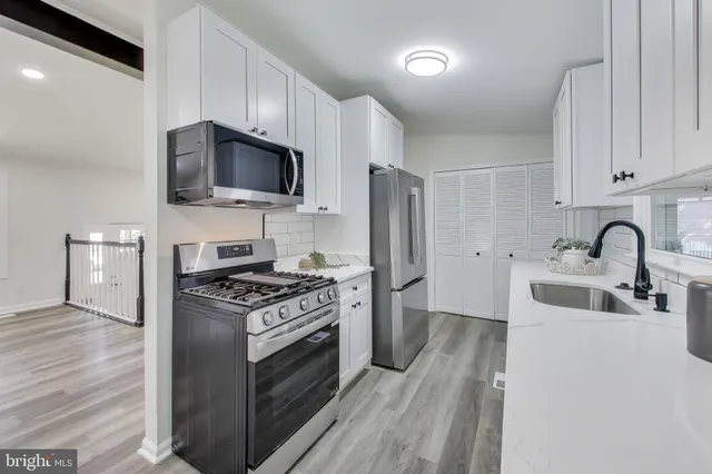 a kitchen with stainless steel appliances a sink a stove top oven a refrigerator cabinets and a dining table with wooden floor