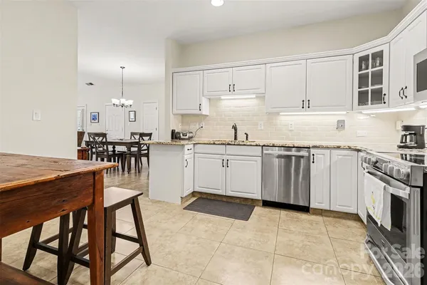 a kitchen with stainless steel appliances granite countertop a stove top oven a sink a dining table and chairs