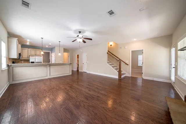 a view of an empty room with wooden floor and kitchen view