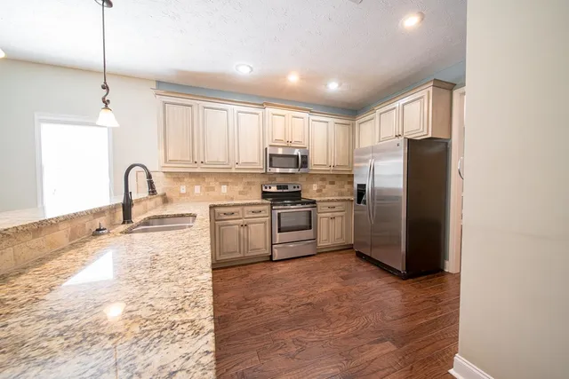 a kitchen with stainless steel appliances granite countertop a refrigerator a sink a stove and white cabinets with wooden floor