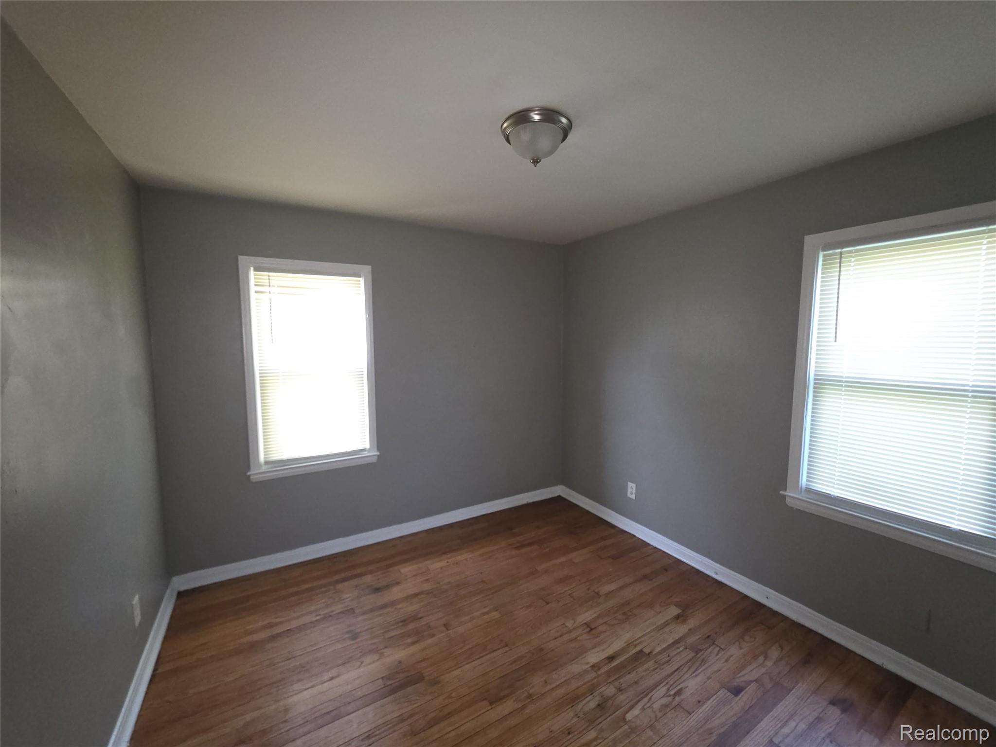 9025 Burt Road Detroit, MI 48228 - Photo 9 of 12 Room featuring wood-finish flooring, two windows with blinds, gray wall finishes, and white trim
