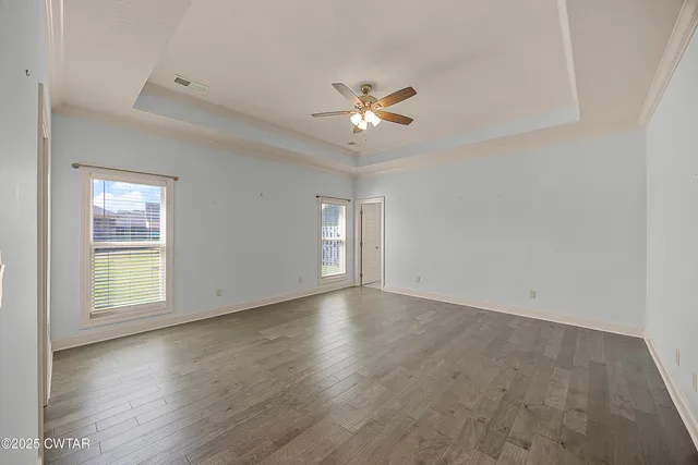 an empty room with wooden floor ceiling fan and windows