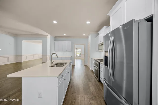 a kitchen with stainless steel appliances a refrigerator a sink a stove and white cabinets